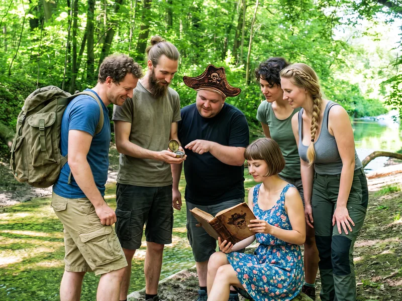 Freundesgruppe mit Kompass und Piratenbuch bei der Schatzsuche an der Mangfall